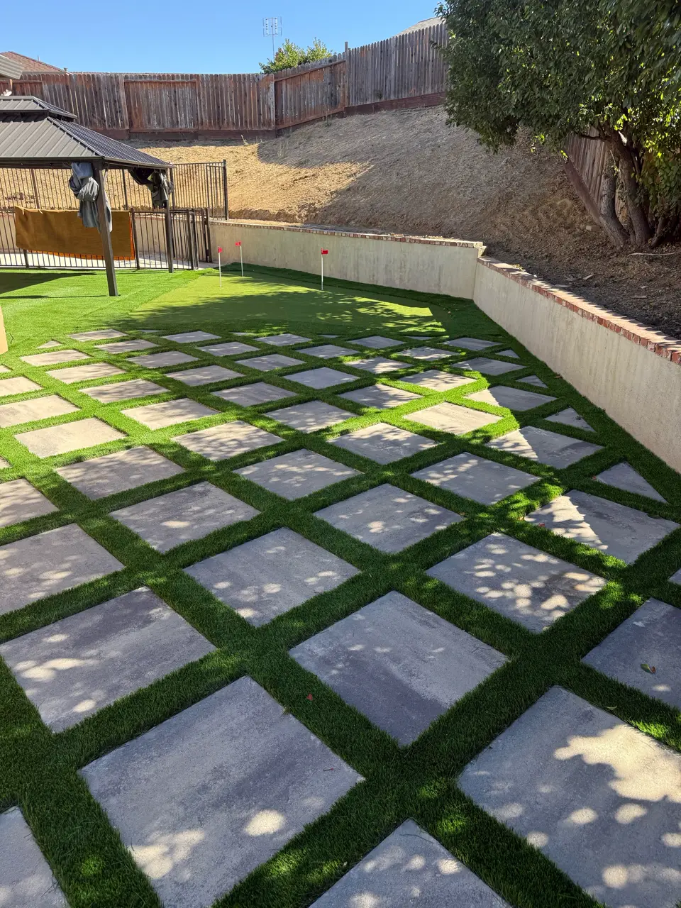 Large-format concrete pavers set in an artificial turf grid beside a block retaining wall